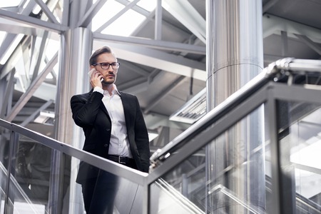 Man on smart phone - young businessman in airport. Handsome serious men wearing suit jacket indoors.の写真素材
