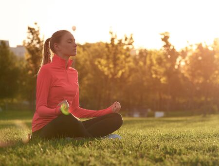 Young woman practice yoga at the sunrise in park.の写真素材