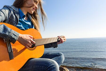 Young woman traveller playing guitar outdoor on sea coast.の写真素材