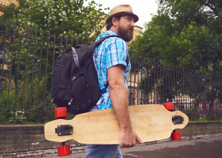 Freaky bearded man walking with longboard in handの写真素材