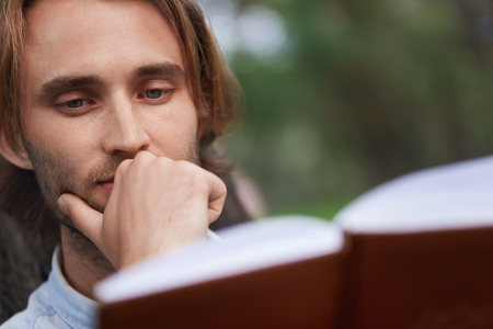 Close up shot. Student in park of campus read a book. Focus on man