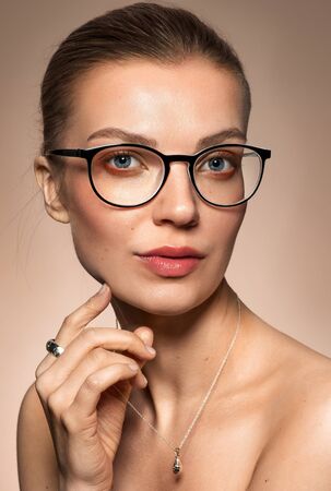 Fashion portrait of young glamour female in optical eyewear with black frame over golden background. Pretty girl with beautiful evening makeup wearing jewelery posing in studioの写真素材
