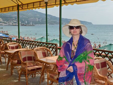 Beautiful woman in a hat and glasses stands on a background of natureの写真素材