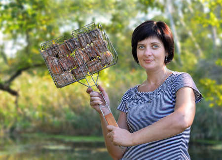 A woman prepares food in nature and keeps the grill with meatの写真素材