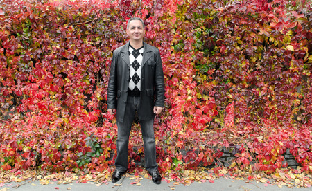 Autumn background. On the walk. A man stands near the leaves of red braiding wild grapeの写真素材