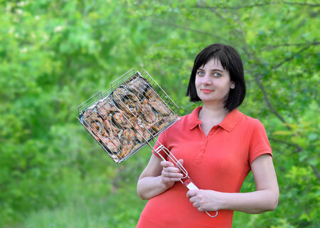Skewers of pieces of fish. Beautiful brunette woman in the woods, nature holds a lattice with fried fishの写真素材