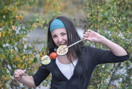Cooking food. Beautiful girl, brunette in a forest in nature keeps vegetables grilled on a skewer.