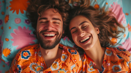 A happy couple in matching pajamas laughs while lying in bed.の素材