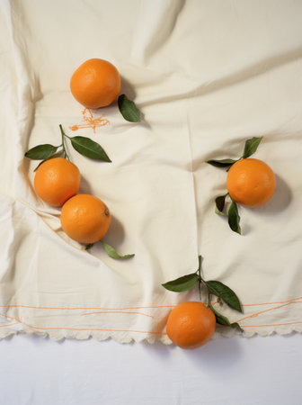eight tangerines on white cloth, with green leaves, everyday ephemera, organic materialの素材