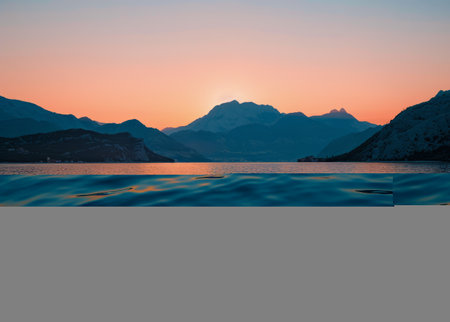 A lake reflecting the colorful hues of the setting sun with towering mountains in the background. The sky is painted with warm tones as the day comes to an end.の素材
