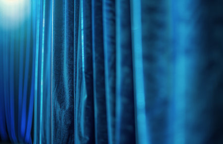 A blue curtain hanging in a room illuminated by several lights, creating a soft and atmospheric glow on the fabric.の素材