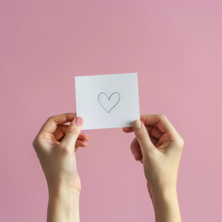 Two hands coming together, holding a piece of paper with a heart drawn on it.の素材