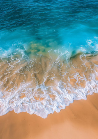 A birds-eye view of a beach shoreline as waves roll in, creating white foam and patterns in the sand.の素材