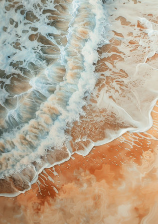 A birds eye view of the ocean waves crashing against the sandy shore.の素材