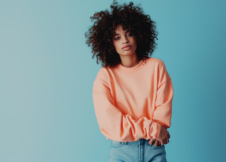 young woman wearing a peach sweatshirt and jeans with curly brown hair,.の素材