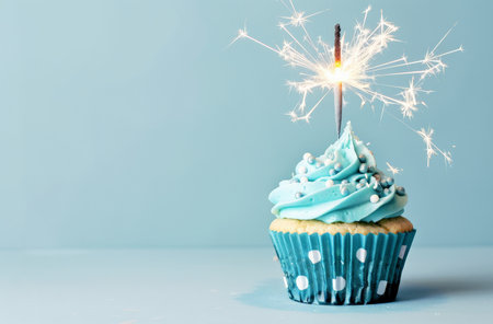 A cupcake topped with vibrant blue frosting and a sparkling sparkler illuminating the scene.の素材