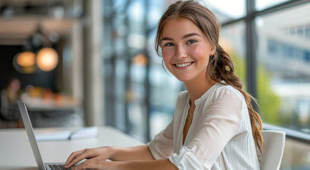 A woman is seated in front of a laptop computer, engaged in work or study.の素材