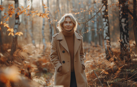 A woman wearing a brown coat stands in an autumn forest, surrounded by colorful leaves and trees.の素材