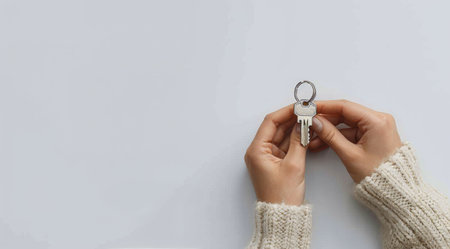 A womans hands hold a silver key with a key ring, isolated on a white background.の素材