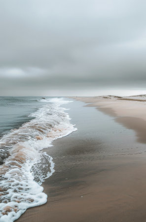 A gentle ocean wave crashes on a sandy beach under a cloudy sky, creating a peaceful and serene atmosphere.の素材