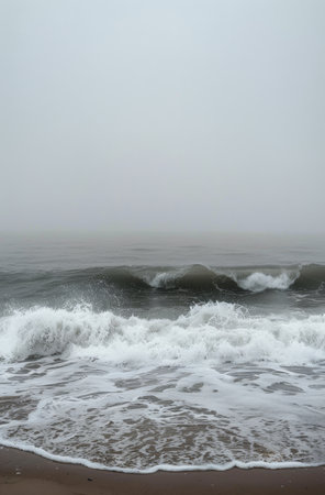 A gentle ocean wave crashes on a sandy beach under a cloudy sky, creating a peaceful and serene atmosphere.の素材