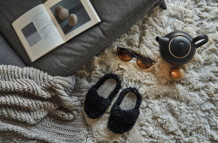 A close-up view of a fluffy white rug with black fuzzy slippers, sunglasses, a black teapot, and a gold orb.の素材