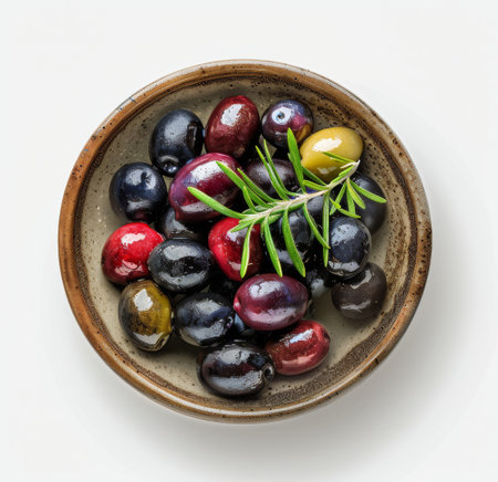 A bowl of olives, including green, black, and red varieties, with a sprig of rosemary on top, on a white background.の素材