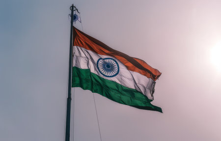 An Indian flag is waving in the wind against a clear blue sky. The flag is brightly colored with the national emblem of India in the center.の素材