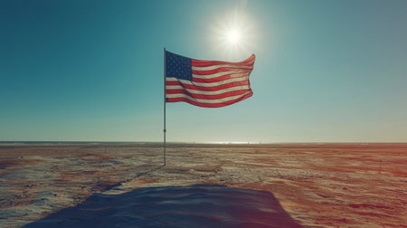 A US flag waving in the wind against a teal sky with plants in the foreground.の素材