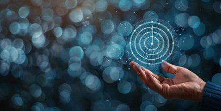 A person's hand holds a blue digital sphere with geometric patterns. The sphere is illuminated and appears to be floating in the air.の素材