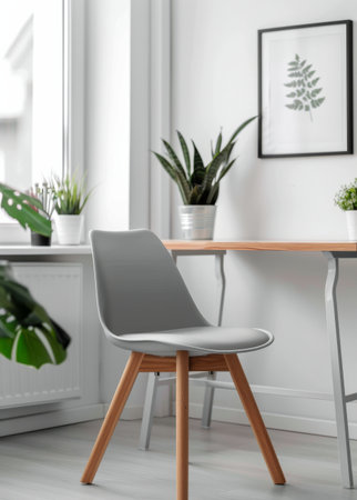 A gray chair with wooden legs sits at a minimalist desk with wooden legs. A notebook rests on the desk, while potted plants and a pencil holder are visible in the background.の素材