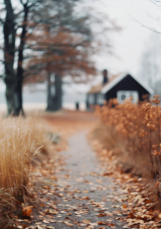 A path covered in fallen leaves leads towards a black cabin in the woods, surrounded by tall trees and a foggy atmosphere. The image has a soft focus, creating a dreamy and melancholic mood.の素材