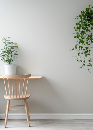 A wooden desk with a laptop on top and a gray chair sits in front of a wall, with a potted plant to the left and a hanging plant to the right.の素材