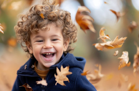 A young boy with curly hair laughs as he is surrounded by falling autumn leaves.の素材