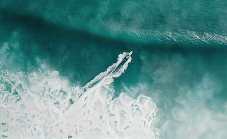 A surfer in a wetsuit rides a wave on a surfboard. The water is blue and the wave is breaking. The image is taken from a high angle, looking down at the surfer.の素材