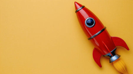 A red toy rocket stands upright on a bright yellow background, ready for liftoff.の素材