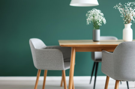 A modern dining room features a wooden table and gray chairs against a vibrant green wall. White pendant lights hang above the table, and a vase of white flowers sits on the table. The room has light wood floors.の素材
