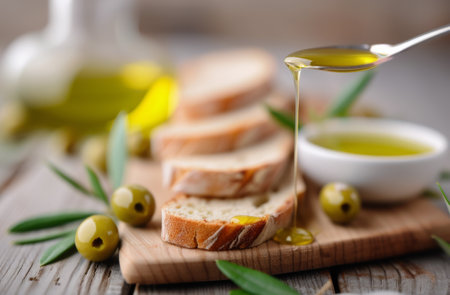 Olive oil being drizzled onto slices of bread on a wooden cutting board. There are green olives and herbs in the background.の素材