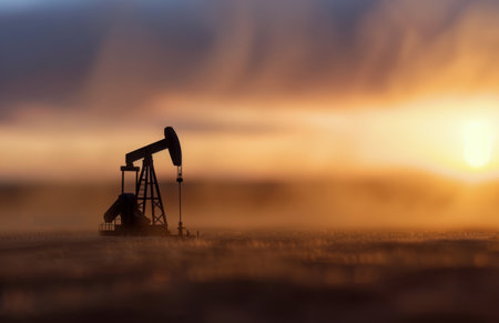 An oil pump stands silhouetted against a hazy sunset, with the sun setting in the distance.の素材