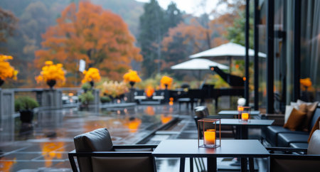 A view of a patio dining area with tables, chairs, and candlelight. The setting is a serene, outdoor space with a view of autumn foliage and a rainy day.の素材
