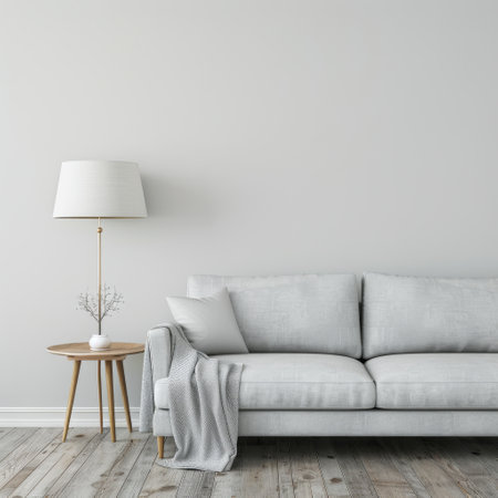 A white sofa sits in a minimalist living room, accented by a round wooden table with a vase of dried branches and a hanging light fixture. The room features light wood floors and a simple white wall.の素材