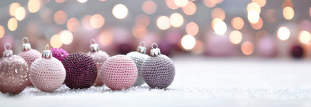 Pink and gray knitted Christmas ornaments sit on a snowy surface with a blurred background of lights.の素材