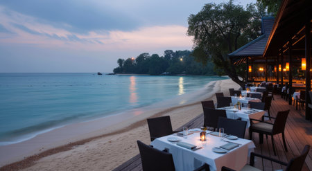 Elegant dining tables are set along a beachfront deck as twilight descends, with flickering candles and a serene ocean view. The atmosphere is inviting, perfect for a romantic evening under the stars.の素材