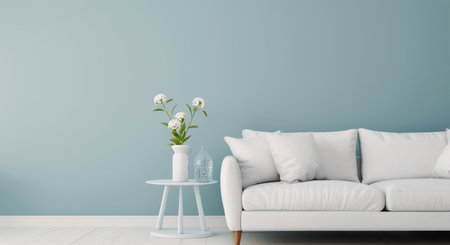A bright living room showcases a light blue wall and a cozy white couch adorned with cushions. A small side table holds a fresh flower arrangement and a glass bottle, enhancing the tranquil atmosphere.の素材