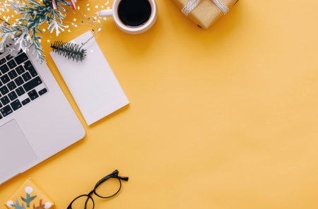A cheerful holiday workspace features a laptop, a steaming cup of coffee, candy canes, wrapped gifts, and festive decorations, set against a vibrant yellow background, creating a warm, inviting atmosphere.の素材