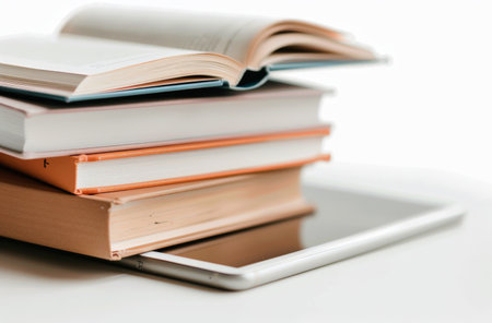 A stack of five colorful books rests on a tablet, with one book opened to display its pages. The setup is in a minimalist workspace, emphasizing simplicity and modern design.の素材