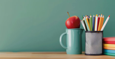 A fresh red apple sits atop a stack of notebooks beside a container filled with various colored pencils, set against a calming green background, conveying a creative and scholarly atmosphere.の素材