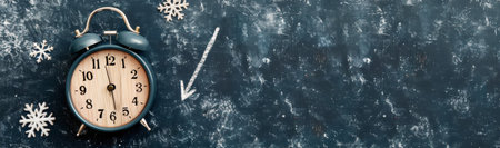 A vintage alarm clock rests on a dark textured surface, accompanied by scattered snowflakes and a directional arrow, creating a winter-themed composition that emphasizes time and seasonal change.の素材