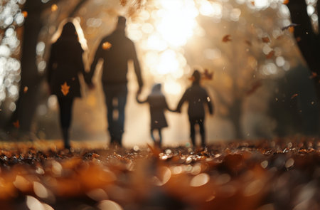 A parent and child walk hand-in-hand along a trail carpeted with autumn leaves, illuminated by the warm glow of the setting sun filtering through the trees.の素材