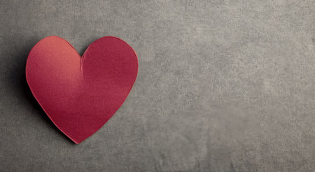 A vibrant red heart cutout rests on a textured gray surface, creating a simple yet striking contrast. The heart embodies warmth and affection, perfect for expressing love on various occasions.の素材